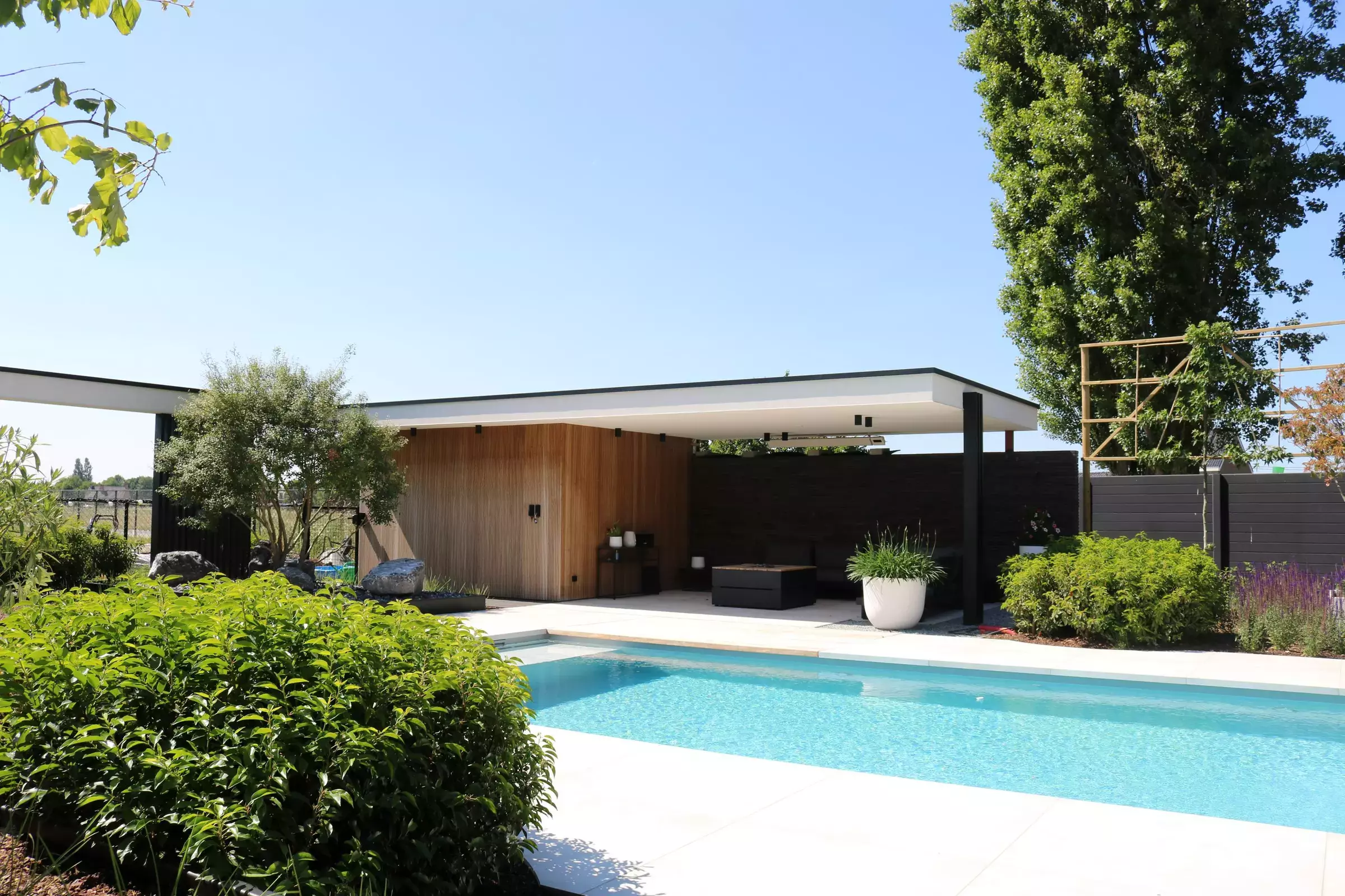 op de voorgtond een wolkmassief met daarchter een zwembad en poolhouse met overdekte zithoek. – foto 1